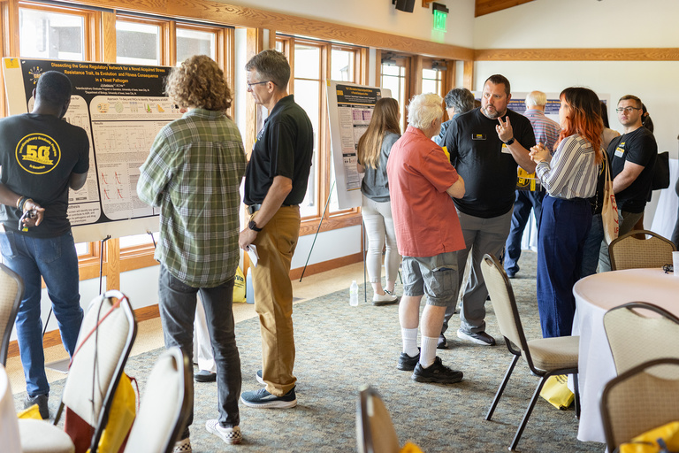 group of alumni and faculty talking, poster session in background