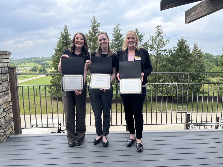 Photo of Jordan Mayberry, Kayla Henry, and Emily Adelizzi holding their poster awards. Brown Deer Golf Course is in the background.